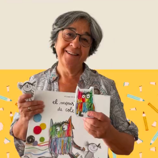 Imagen tipo retrato de Mónica, quien en redes sociales se hace llamar abuela pediatra. Mira a la cámara mientras sostienen un libro llamado "El monstruo de colores"